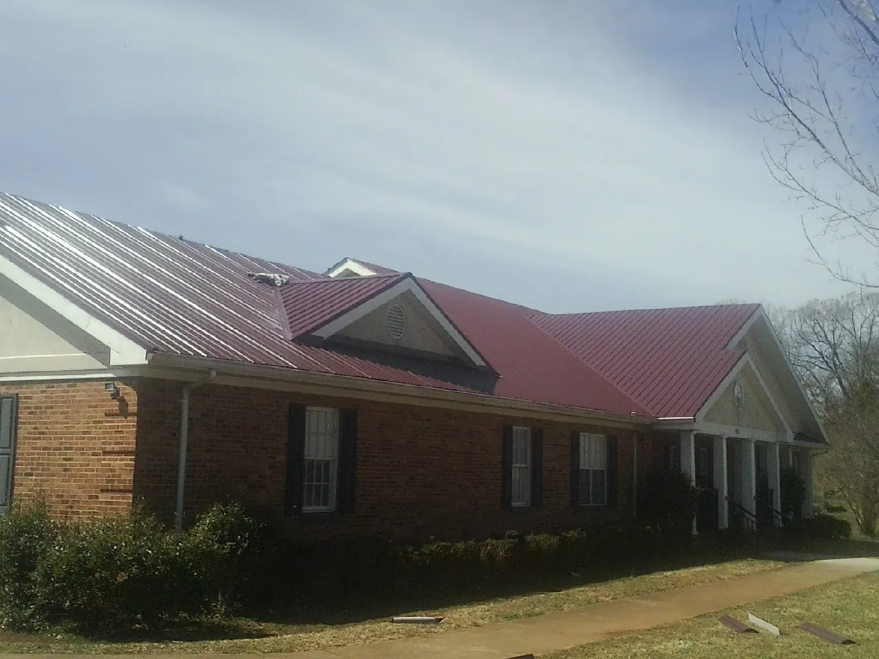 Red metal roof with gabled entries on a long brick building, from a Hail Damage Roof Repair job in Amity